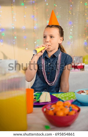 Girl blowing party horn during birthday party at home