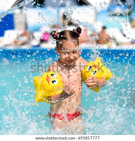 A bright sunny photo of a smiling little girl enjoying playing and swimming in the open pool