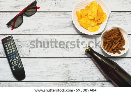 Relaxing at home with a good movie - flat lay with bottle of beer, different snacks, remote control and tv glasses. Party for one concept.