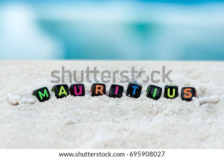 Word Mauritius is made of multicolored letters on snow-white sand against the blue sea. Tourism, rest, resort, sea, sun, beach