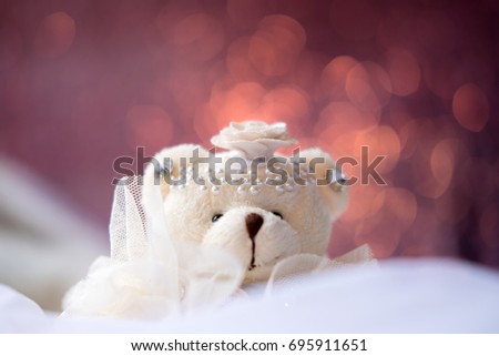Closeup image of small teddy bear doll sitting on white carpet with blur pink color bokeh background