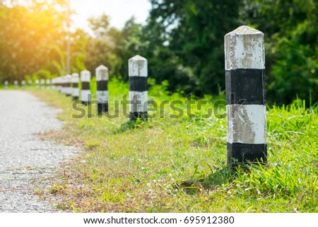 Milestones - Black and white milestones with green grass roadside, Trees roadside in background . concept for next step. Next station.Up level. Royalty-Free Stock Photo #695912380