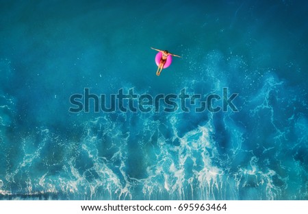 Aerial view of young woman swimming on the pink swim ring in the transparent turquoise sea in Oludeniz,Turkey. Summer seascape with girl, beautiful waves, blue water in sunny day. Top view from drone