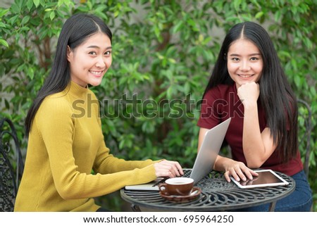 Two students teen girls studying together on line with a laptop in the garden with green tree background.