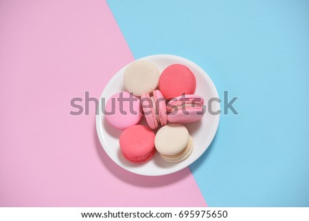 French colorful macarons in white ceramic dish on blue and pink pastel background. Romantic concept with copy space for design work. Sweet dessert for tea or coffee time. Idea for creative card.