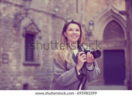 Young cheerful woman with camera looking curious and taking pictures outdoors