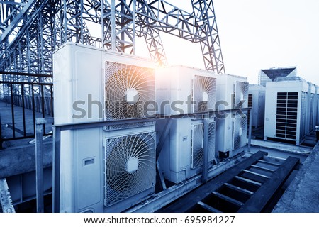 Air conditioner units (HVAC) on a roof of industrial building with blue sky and clouds in the background. Royalty-Free Stock Photo #695984227