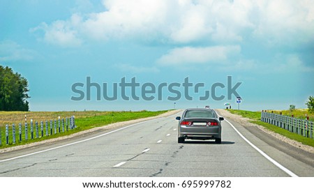 Rear view of a car speeding on asphalt road in countryside to escape summer thunderstorm.  Cloudy, stormy sky. Road signs along the route. Royalty-Free Stock Photo #695999782