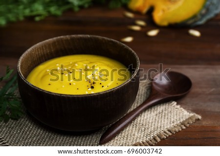 Wooden bowl of vibrant yellow pumpkin soup with spoon on table. Rustic food background. Thanksgiving, concept. Text space