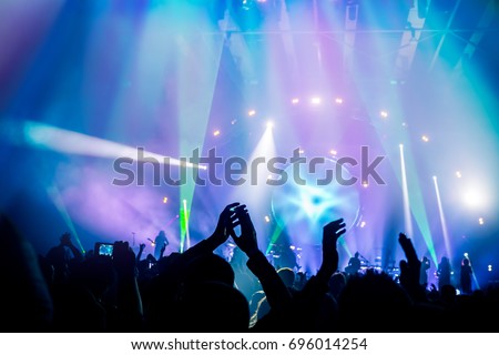 Many people enjoying concert, band performs on stage in the bright blue light, people enjoying music, dancing with raised up hands and clapping, active night life 