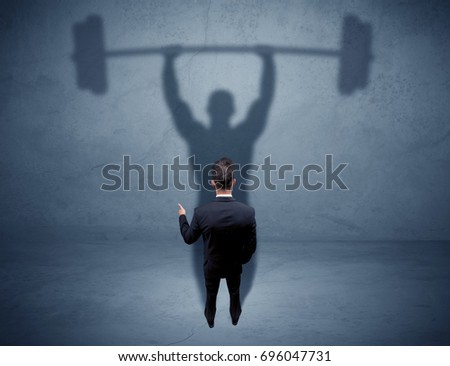 A confident young elegant salesman with briefcase facing a wall, looking at his strong, weight lifting shadow concept