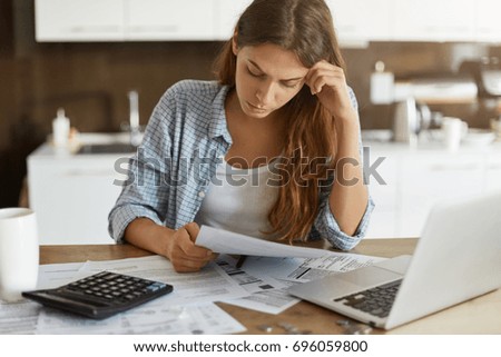 Portrait of worried young single mother feeling stressed while working through finances in kitchen late at night, thinking how to pay off debts for rent and domestic bills. Financial problems concept Royalty-Free Stock Photo #696059800
