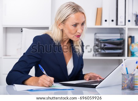 Successful businesswoman concentrated on work with papers and laptop in office