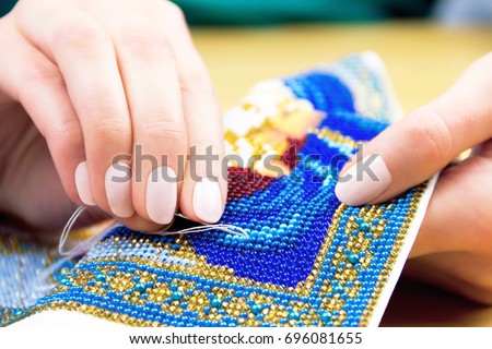 Hands of woman / female / girl bead embroidery ornament towel on wooden background Royalty-Free Stock Photo #696081655