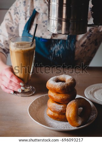 Pishki - Russian Doughnuts. Girl dusting sugar powder on Doughnuts, girl drinking cocoa in a tall transparent glass on a background in a traditional canteen. Vertical photo