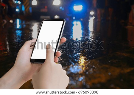 hand hold mobile blank screen and water on street and color lighting, traffic night illuminated reflection liquid,using the car on the road when it weather rainy season accident, copy space the right.