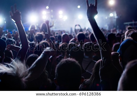 silhouettes of people at a concert in front of the scene in bright light.