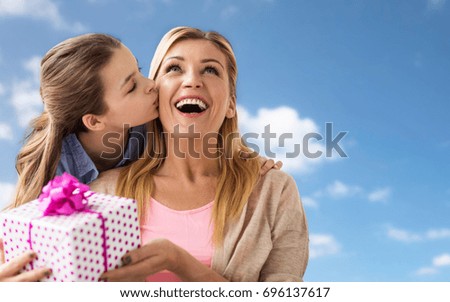 people, holidays and family concept - happy girl giving birthday present to mother over blue sky and clouds background