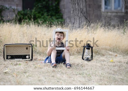 Hipster child with retro vintage radio. Little boy listens to music through an old radio. Child, old radio, lamp and picture frame