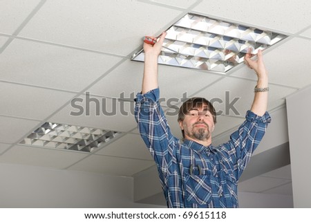 Electrician installs lighting to the ceiling in the office.