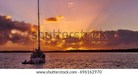 Surreal orange cumulonimbus cloud sunrise at sea with angel rays and a yacht in silhouette.
The photograph was taken at Tin Can Bay, Queensland, Australia.

