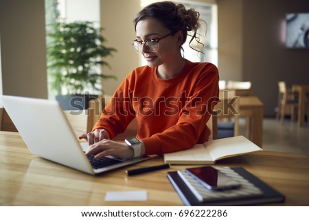 Professional young copywriter in trendy eyewear working on creation advertising content typing on laptop computer connected to wireless internet, skilled journalist browsing information in web site Royalty-Free Stock Photo #696222286
