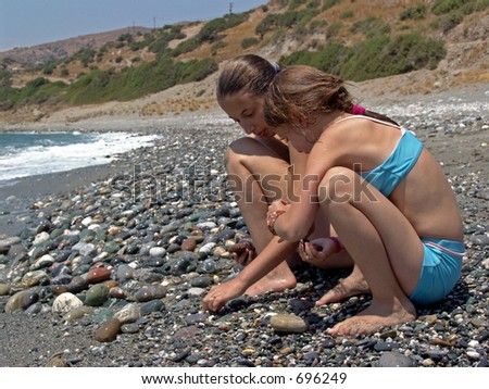 Two young girls collecting stones on a Mediterranean beach in Crete