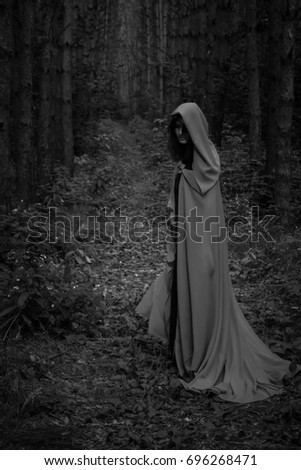 Halloween concept. A witch in a black robe. Among the forest. Photo for your design. Vertical sheet orientation