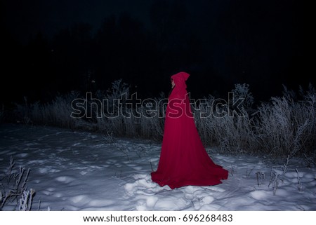Halloween concept. Witch in red against the background of fallen snow. Night and witchcraft. O for your design