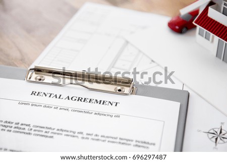 Rental agreement contract paper with blueprints and house model on the table - property and real estate concept