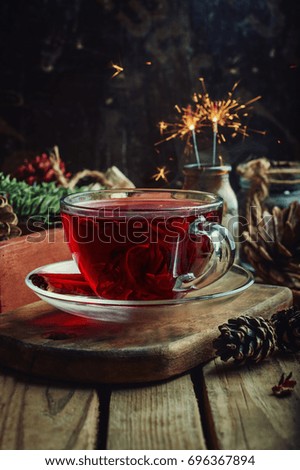 Red tea with spices (cinnamon and anise) in a glass cup on a sturdy background, concept of a Christmas card, effect of Bengal lights
