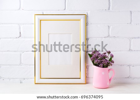 Gold decorated frame mockup with purple field flowers in polka dot pink rustic pitcher vase. Empty frame mock up for presentation artwork. Template framing for modern art.