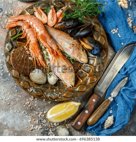Image of fish, shrimp, shellfish on ceramic plate at table with lemon, knives, seashells