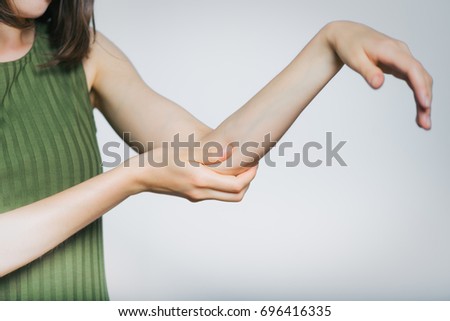 Beautiful young woman has pain in elbow, isolated on gray background