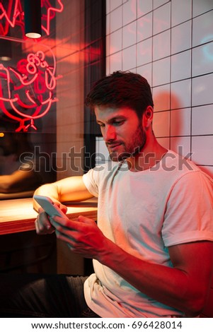 Picture of caucasian young attractive serious man sitting in cafe looking aside chatting by phone.