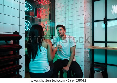 Picture of young multiethnic smiling loving couple sitting in cafe drinking beer. Looking aside.