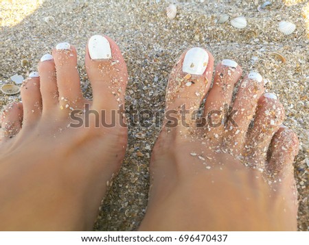 Beautiful fingers of a young girl. White nail polish. Pedicure. The background is a sandy beach. A hot, sunny day.