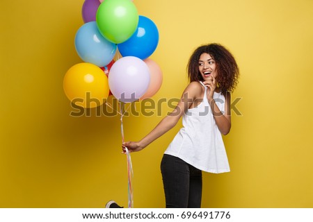 Celebration Concept - Close up Portrait happy young beautiful african woman with white t-shirt running with colorful party balloon. Yellow Pastel studio Background.