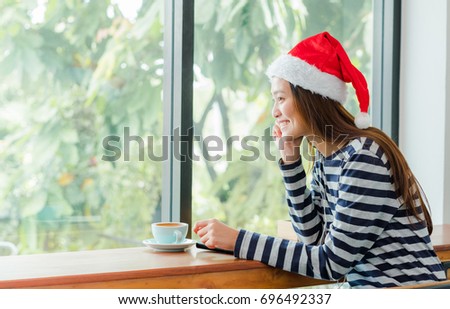 Asian teenage girl with Christmas hat and smile face resting her chin on her hands and drink coffee near window in xmas party at cafe ,Celebrate New year and Christmas holiday concept.