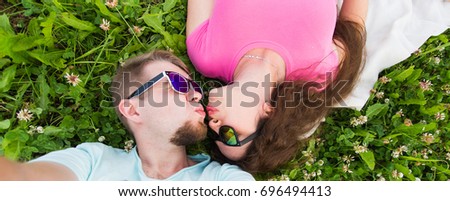 Summer, love and people concept - happy teenage couple in sunglasses lying on grass and taking selfie on smartphone
