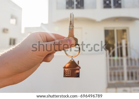 Holding house keys on house shaped keychain closeup in front of a new home. Concept of real estate Royalty-Free Stock Photo #696496789
