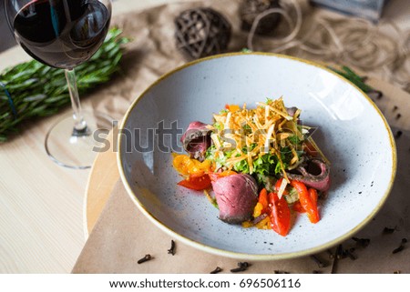 Close-up of salad with beef, cherry tomatoes, pepper, lettuce, background of a glass of red wine, rosemary, beautiful trendy serve, restaurant, dinner, lunch, delicious food, high-cuisine