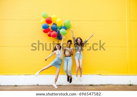 Picture of young happy women friends standing over yellow wall. Have fun with balloons. Royalty-Free Stock Photo #696547582