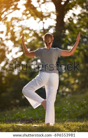 Woman exercising body balance exercises in forest, back view