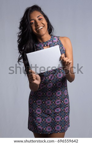 The hands hold a white banner with space for text. Brazilian woman of mixed race ethnicity wearing colorful purple dress with floral pattern. Summer. Tropical make up.