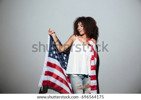 Happy patriotic african woman holding US flag while standing isolated over gray background