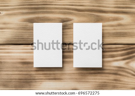 Closeup mockup of two white blank vertical business cards at light natural wooden background.