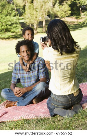 Mother photographing son and husband with digital camera in park.