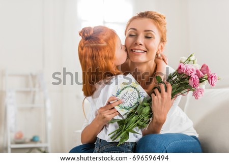 adorable girl greeting mother with bouquet of flowers and postcard on mothers day at home