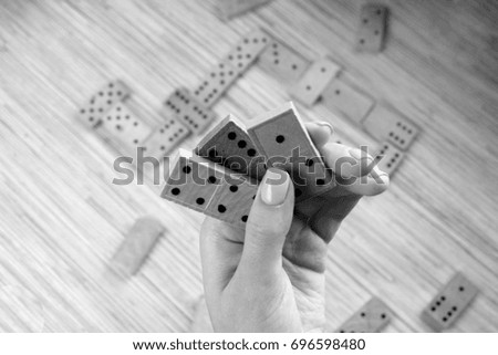  Domino game. Women hand is holding three pieces of domino. Background is full with domino